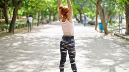 Photo for Young redhead woman wearing sportswear stretching arms at park - Royalty Free Image