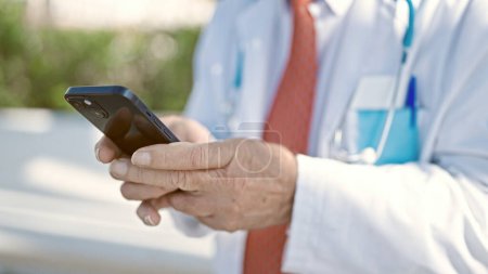 Téléchargez les photos : Senior homme aux cheveux gris médecin en utilisant smartphone au parc - en image libre de droit