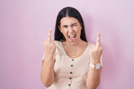 Foto de Young hispanic woman standing over pink background showing middle finger doing fuck you bad expression, provocation and rude attitude. screaming excited - Imagen libre de derechos