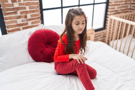 Photo for Adorable hispanic girl suffering for knee injury sitting on bed at bedroom - Royalty Free Image