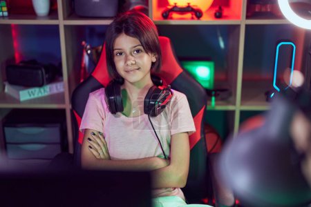 Foto de Adorable chica hispana serpenteante sonriendo confiada sentada con los brazos cruzados gesto en la sala de juegos - Imagen libre de derechos