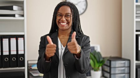 Foto de Trabajadora de negocios afroamericana sonriendo confiada haciendo un gesto de pulgares hacia arriba en la oficina - Imagen libre de derechos