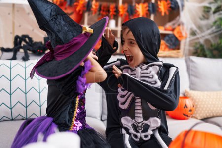 Foto de Adorable chico y chica teniendo fiesta de Halloween haciendo gesto de miedo en casa - Imagen libre de derechos