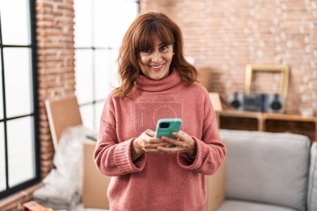 Téléchargez les photos : Middle age woman smiling confident using smartphone at new home - en image libre de droit