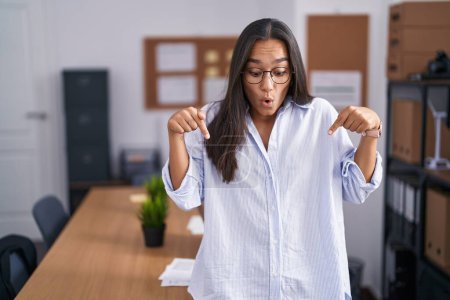 Photo for Young hispanic woman at the office pointing down with fingers showing advertisement, surprised face and open mouth - Royalty Free Image