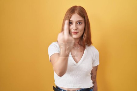 Photo for Young redhead woman standing over yellow background showing middle finger, impolite and rude fuck off expression - Royalty Free Image