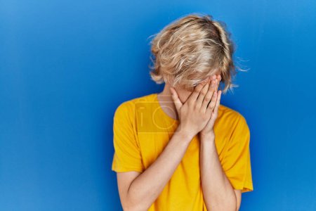 Photo for Young modern man standing over blue background with sad expression covering face with hands while crying. depression concept. - Royalty Free Image