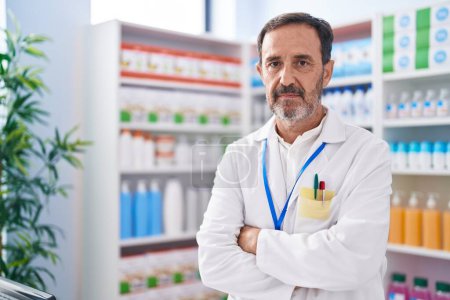 Téléchargez les photos : Homme moyen pharmacien debout avec les bras croisés geste à la pharmacie - en image libre de droit