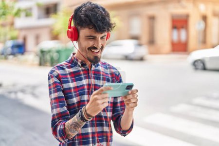 Téléchargez les photos : Young hispanic man smiling confident playing video game at street - en image libre de droit
