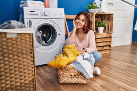 Foto de Joven mujer caucásica sonriendo ropa de lavado segura en la sala de lavandería - Imagen libre de derechos