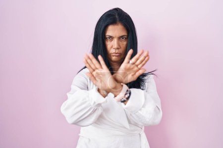 Foto de Mujer hispana madura de pie sobre fondo rosa expresión de rechazo cruzando brazos y palmas haciendo signo negativo, cara enojada - Imagen libre de derechos