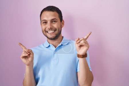 Téléchargez les photos : Homme hispanique debout sur fond rose souriant confiant pointant avec les doigts vers différentes directions. espace de copie pour la publicité - en image libre de droit