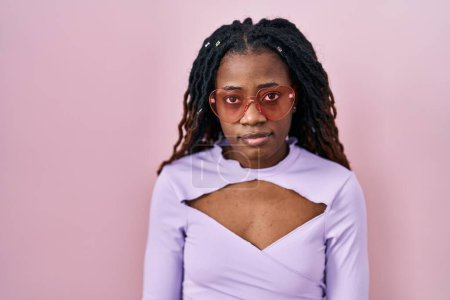 Photo for African woman with braided hair standing over pink background relaxed with serious expression on face. simple and natural looking at the camera. - Royalty Free Image