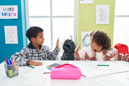 Téléchargez les photos : Adorable afro-américain garçon et fille élèves dessin sur ordinateur portable haute cinq à la classe - en image libre de droit