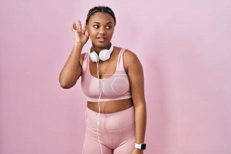 Photo for African american woman with braids wearing sportswear and headphones smiling with hand over ear listening an hearing to rumor or gossip. deafness concept. - Royalty Free Image