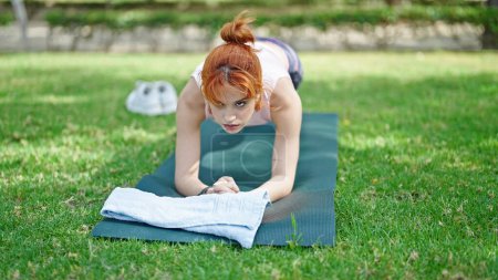 Foto de Mujer pelirroja joven entrenamiento abs ejercicio en el parque - Imagen libre de derechos