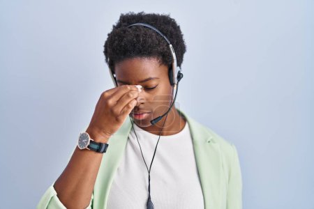 Foto de Mujer afroamericana con auriculares de agente de centro de llamadas cansada frotando la nariz y los ojos sintiendo fatiga y dolor de cabeza. concepto de estrés y frustración. - Imagen libre de derechos