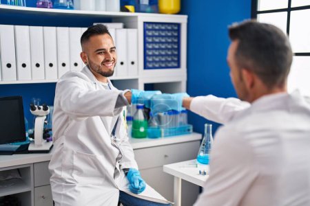 Photo for Two men scientists smiling confident bump fists at laboratory - Royalty Free Image