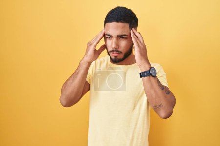 Photo for Young hispanic man standing over yellow background with hand on head, headache because stress. suffering migraine. - Royalty Free Image