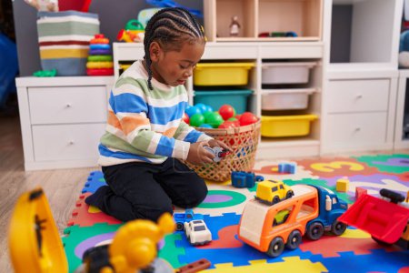Téléchargez les photos : Africain américain garçon jouer avec voiture jouet assis sur le sol à la maternelle - en image libre de droit