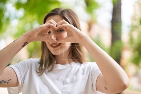 Téléchargez les photos : Jeune femme souriante confiante faire geste de coeur avec les mains au parc - en image libre de droit