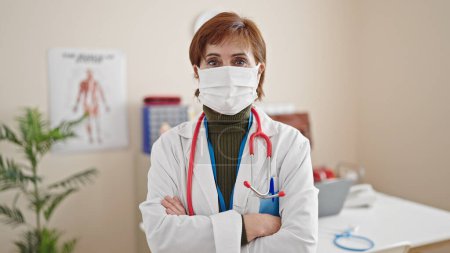 Photo for Mature hispanic woman doctor standing wearing medical mask at clinic - Royalty Free Image