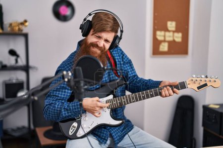 Foto de Joven pelirroja músico cantando canción tocando la guitarra eléctrica en el estudio de música - Imagen libre de derechos