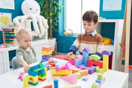 Foto de Adorable niño y niña jugando con bloques de construcción sentado en la mesa en el jardín de infantes - Imagen libre de derechos