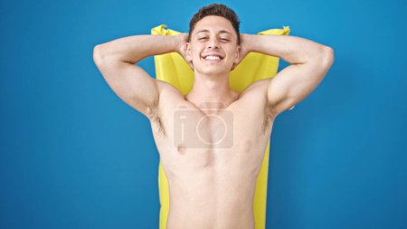Foto de Joven turista hispano sonriendo confiado relajado en hamaca inflable de la piscina sobre fondo azul aislado - Imagen libre de derechos