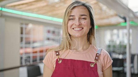 Téléchargez les photos : Jeune femme blonde serveuse souriante confiante debout sur la terrasse du café - en image libre de droit