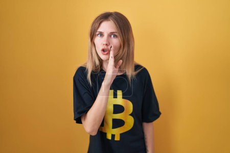Photo for Blonde caucasian woman wearing bitcoin t shirt hand on mouth telling secret rumor, whispering malicious talk conversation - Royalty Free Image