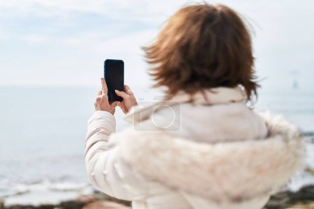 Foto de Middle age woman make photo by smartphone at seaside - Imagen libre de derechos