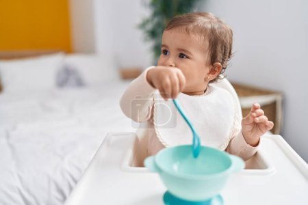 Photo for Adorable hispanic baby holding spoon sitting on highchair at bedroom - Royalty Free Image