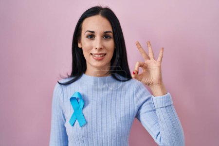Téléchargez les photos : Femme hispanique portant un ruban bleu faisant signe ok avec les doigts, souriant geste amical excellent symbole - en image libre de droit