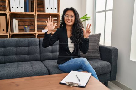 Photo for Young asian woman at consultation office showing and pointing up with fingers number eight while smiling confident and happy. - Royalty Free Image