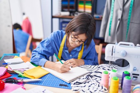 Foto de Adorable sastre de chica hispana dibujando en cuaderno en fábrica de ropa - Imagen libre de derechos