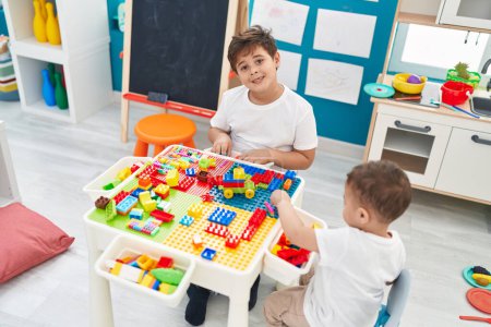 Foto de Adorables niños jugando con bloques de construcción sentados en la mesa en el jardín de infantes - Imagen libre de derechos