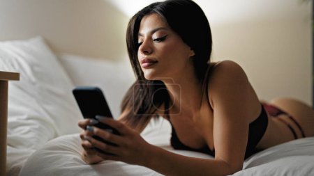 Foto de Mujer joven caucásica usando lencería usando smartphone en el dormitorio - Imagen libre de derechos