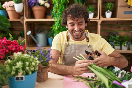 Téléchargez les photos : Jeune homme hispanique fleuriste faire bouquet de fleurs coupant tige à la boutique de fleurs - en image libre de droit