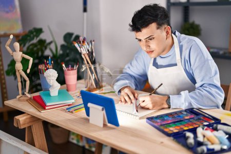 Téléchargez les photos : Jeune artiste homme non binaire utilisant le dessin tactile sur ordinateur portable au studio d'art - en image libre de droit