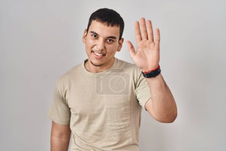 Téléchargez les photos : Jeune homme arabe portant t-shirt décontracté renonçant à dire bonjour heureux et souriant, geste de bienvenue amical - en image libre de droit