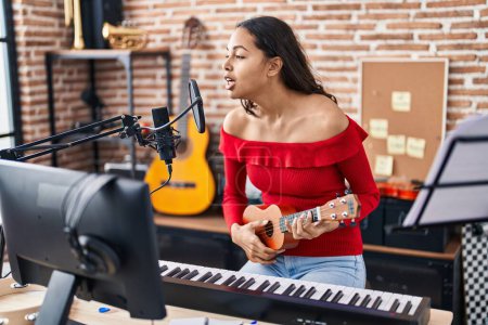 Photo for Young african american woman musician singing song playing ukelele at music studio - Royalty Free Image