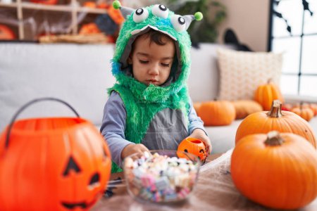 Téléchargez les photos : Adorable garçon hispanique ayant fête d'Halloween tenant des bonbons à la maison - en image libre de droit