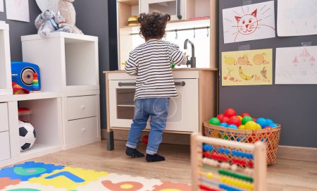 Photo for Adorable hispanic girl playing with play kitchen standing at kindergarten - Royalty Free Image