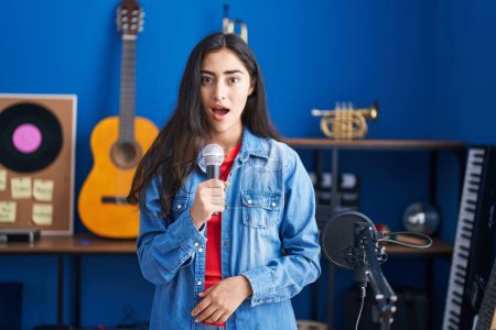 Téléchargez les photos : Jeune adolescente chantant chanson à l'aide d'un microphone effrayé et étonné avec la bouche ouverte pour la surprise, visage incrédule - en image libre de droit