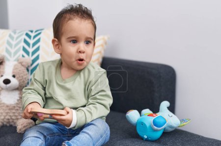 Foto de Adorable chico hispano jugando con juguete sentado en el sofá en casa - Imagen libre de derechos