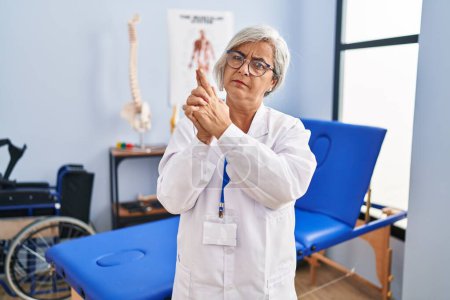 Photo for Middle age woman with grey hair working at pain recovery clinic holding symbolic gun with hand gesture, playing killing shooting weapons, angry face - Royalty Free Image