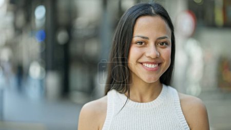 Foto de Joven hermosa mujer hispana sonriendo confiada de pie en la calle - Imagen libre de derechos
