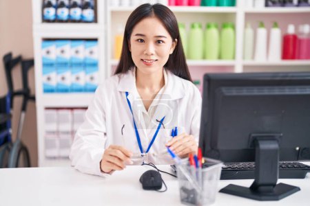 Photo for Young chinese woman pharmacist smiling confident holding glasses at pharmacy - Royalty Free Image