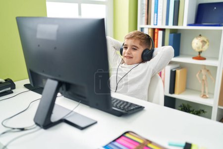 Photo for Adorable hispanic boy student using computer and headphones relaxing with hands on head at classroom - Royalty Free Image